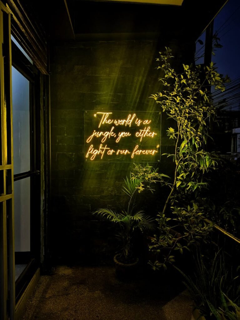 Neon text in a dark corner creates a moody atmosphere with plants.